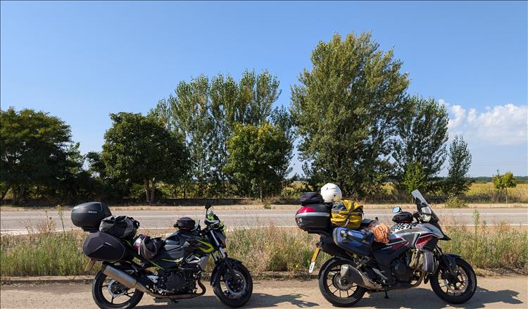 The 2 bikes with luggage, some trees and dried grass fields in the sunshine near Leon