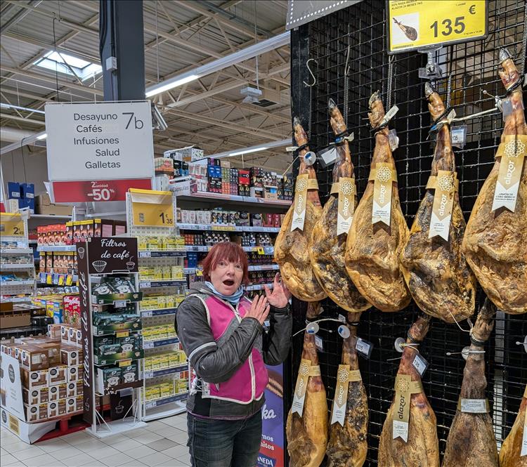 Giant hams hang from a rack and Sharon puts on a fake surprised face