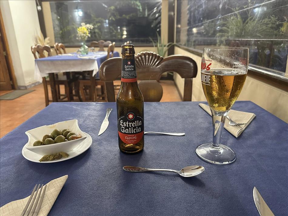 A bottle of beer, some poured into a glass and a small dish of olives in a restauarant
