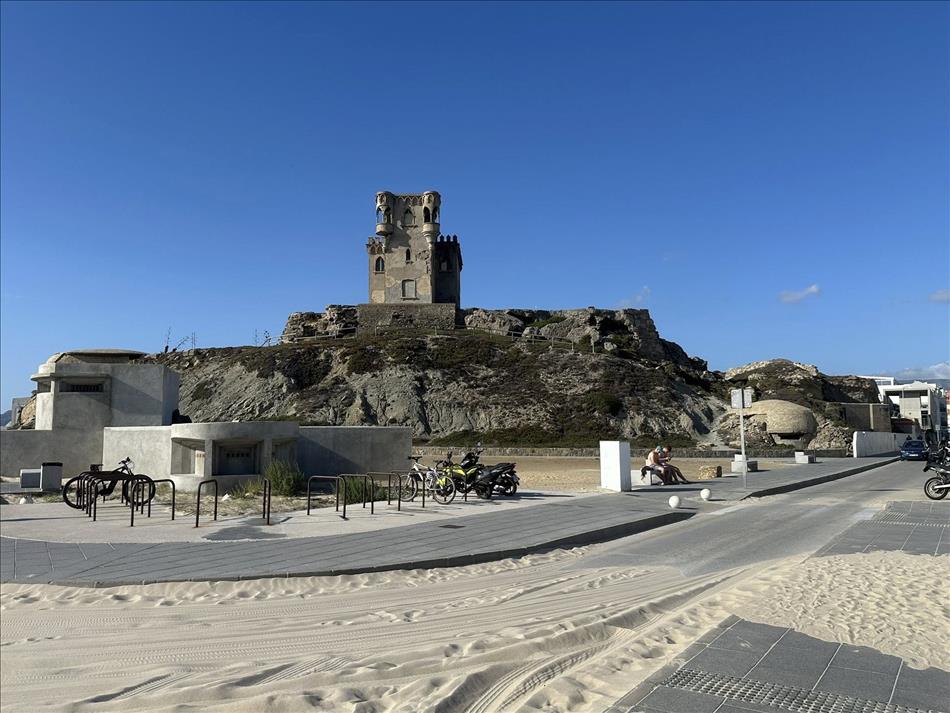Peculiar stylished tower or micro castle atop a hillock. There's sand and a public area