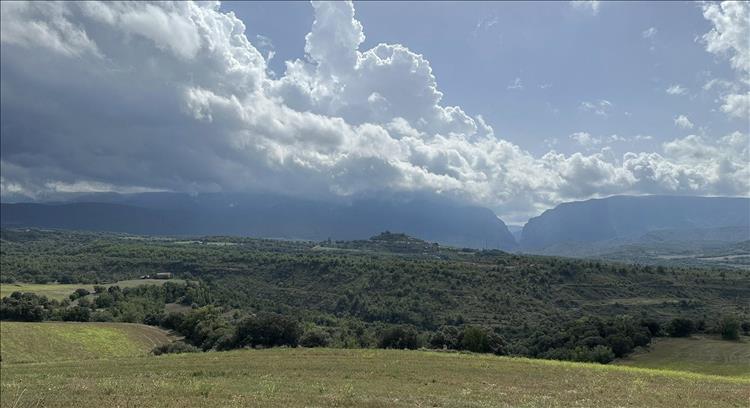 A vast tumultuous cloud front above a range of mountains and trees