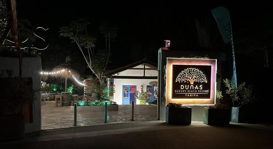 An illuminated sign reads dunas beach resort, in the dark we see a few buildings