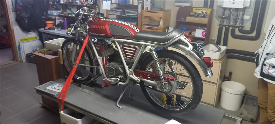 A small classic racing motorcycle strapped to a motorcycle lift in the garage