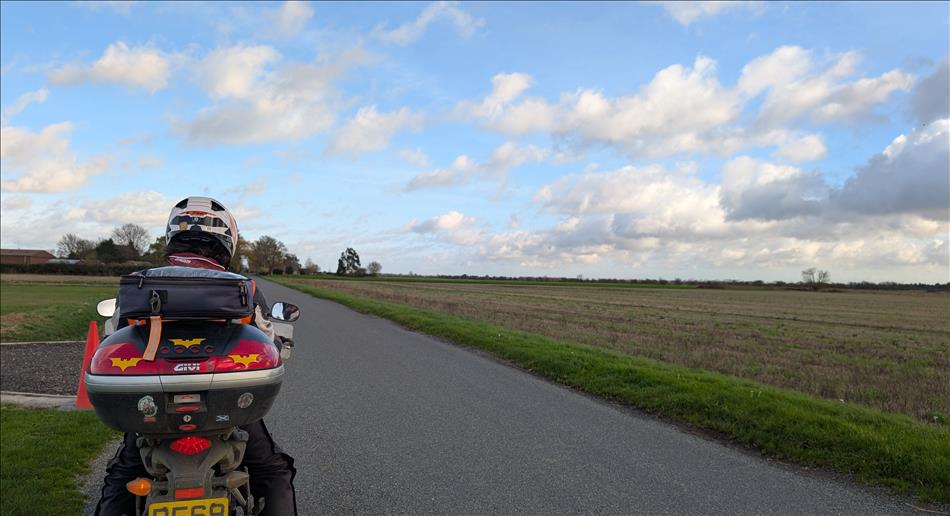 Blue skies with a few light clouds, flat farming countryside, and Ren on his bike