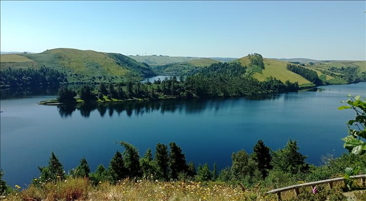 Green hills and trees surround a lake in the hills on a glorious blue sky day
