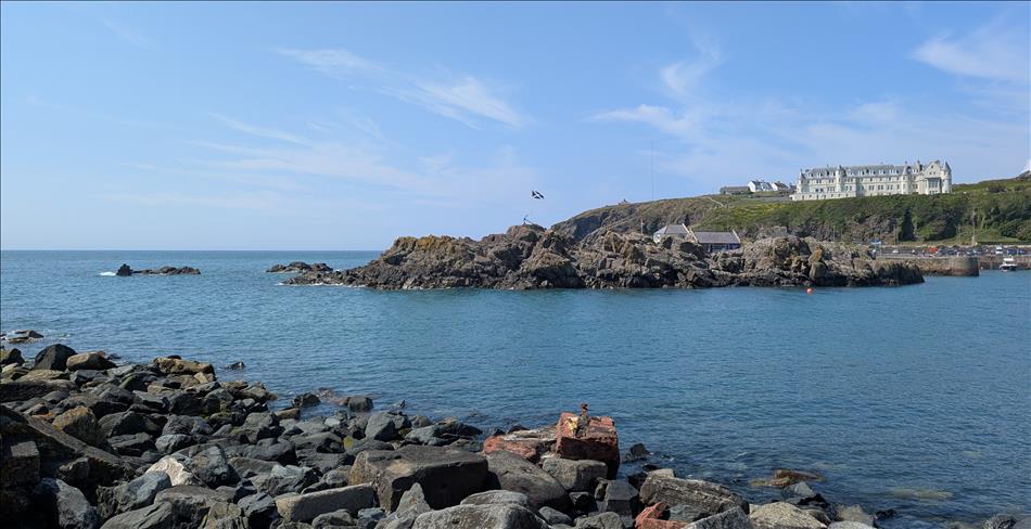 Rocky angular shoreline, a white hotel on the cliffs, and the sea under blue skies