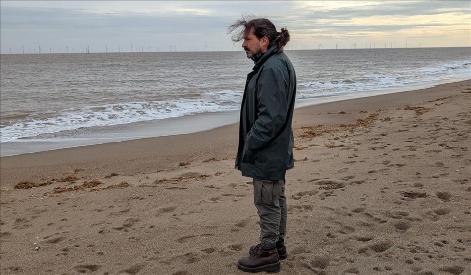 Ren on a windy, cold and rainy beach looking like he's thinking