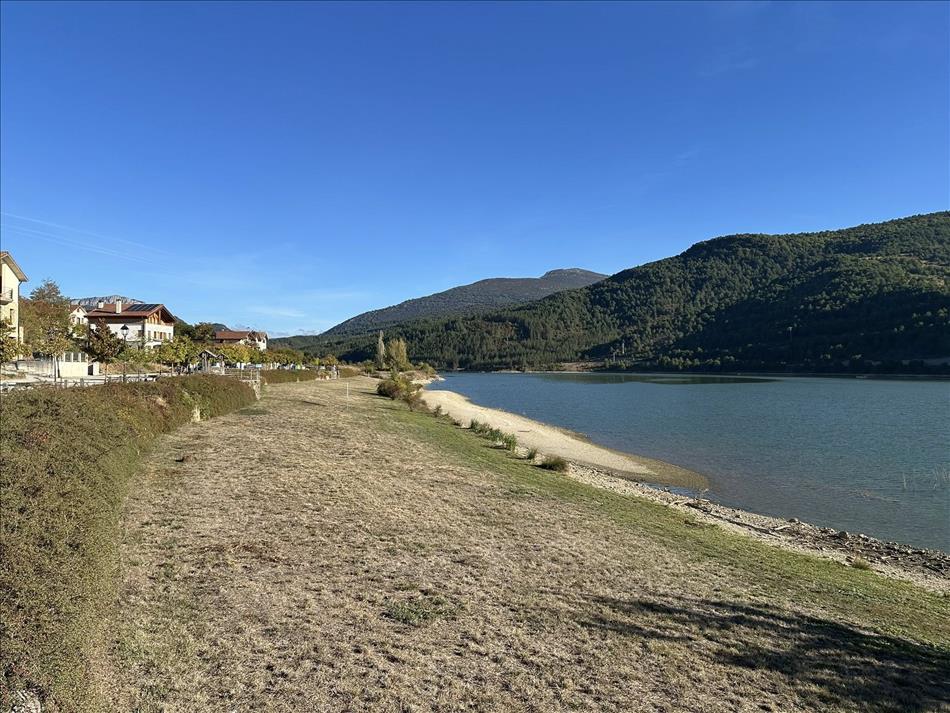 The shore of a reservoir with trimmed grass, smart houses to the left, hills to the right