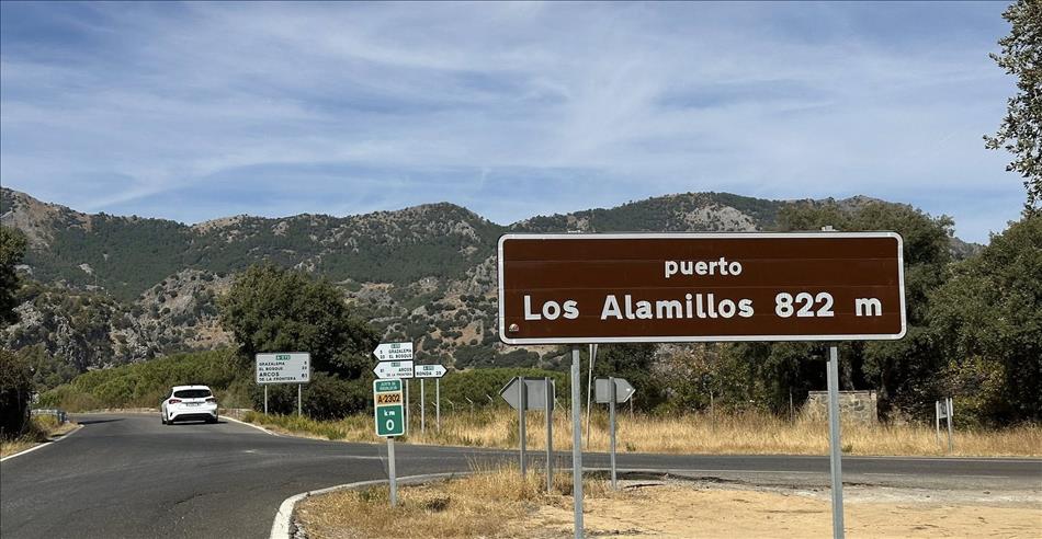 Rocky mountain tops but with some trees, the road and street signs
