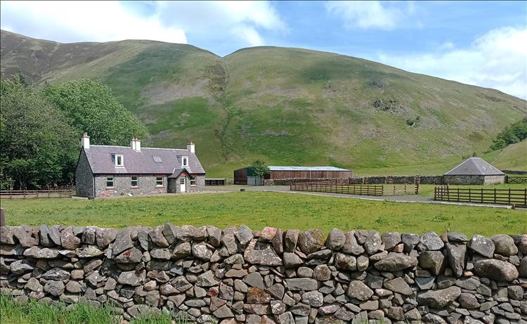 A large stone cottage and a long low barn amid the big ominous mountains and skies at Talla