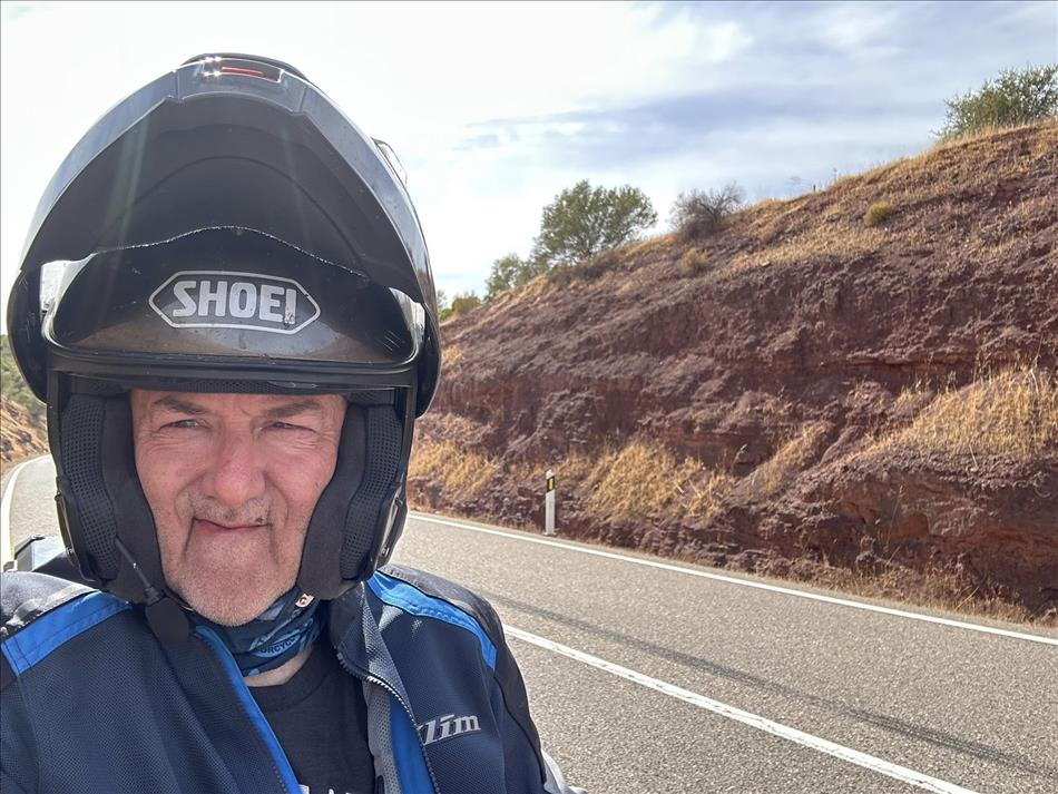 Selfie of Andy with helmet flipped up. The rocks behind are the same dark dusky red colour