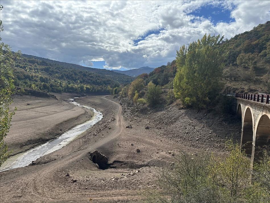 A dried up reservoir with the current bridge and the washed out remains of a bridge and track below