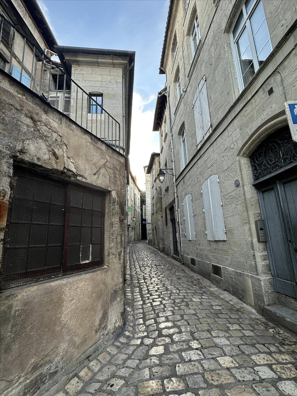 A very narrow cobbled street with tall light grey stone buildings imposing above
