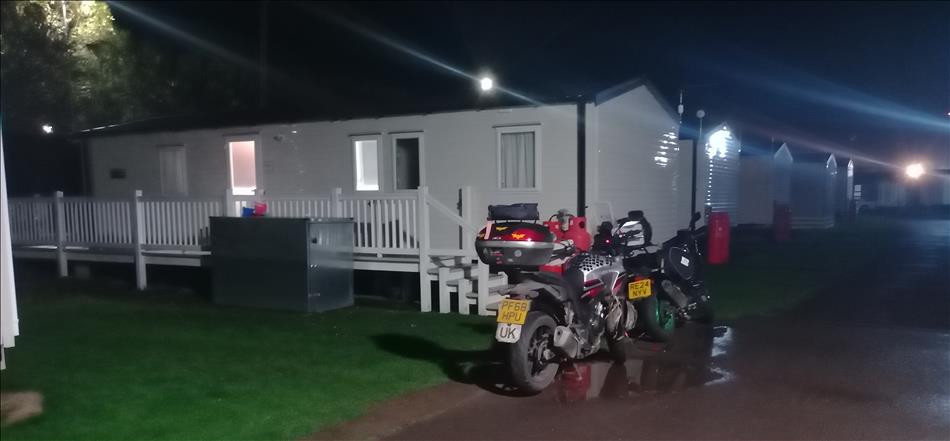 A static caravan seen from outside in the dark with 2 motorcycles close by