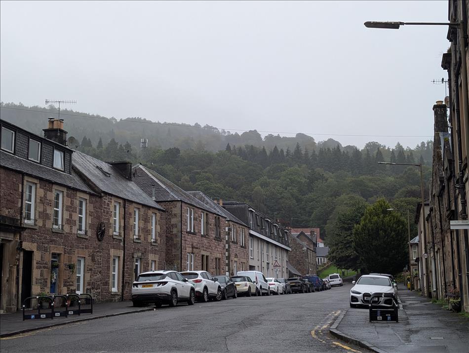 Stone houses by the road, beyond the hill rises covered in thick woodland