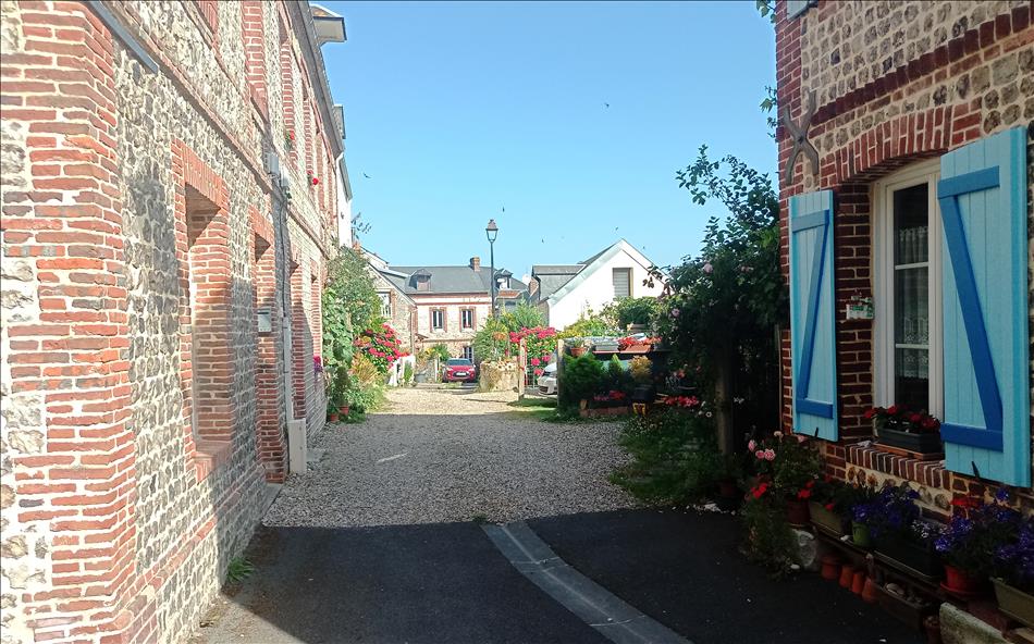 Brick and flint French houses along a gravel street with flowers on windows and borders