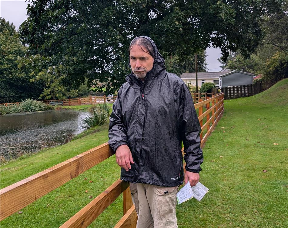 Ren pulls a grumpy face while sodden in the rain with trees and a pond behind him