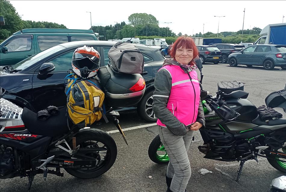 Sharon smiling in her bright pink vest over her bike gear, in front of the bikes at Keele Services