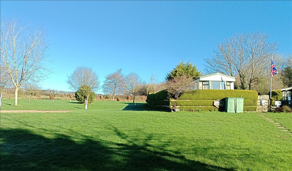 Trimmed grass on various levels, a static caravan behind a bush, trees and clear skies