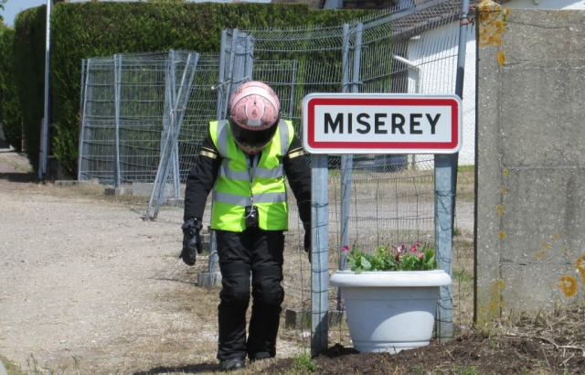 Sharon with her head down next to a French town sign called misery