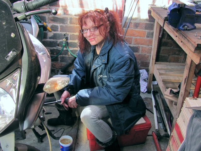 Sharon in the shed fixing a motorcycle and smiling