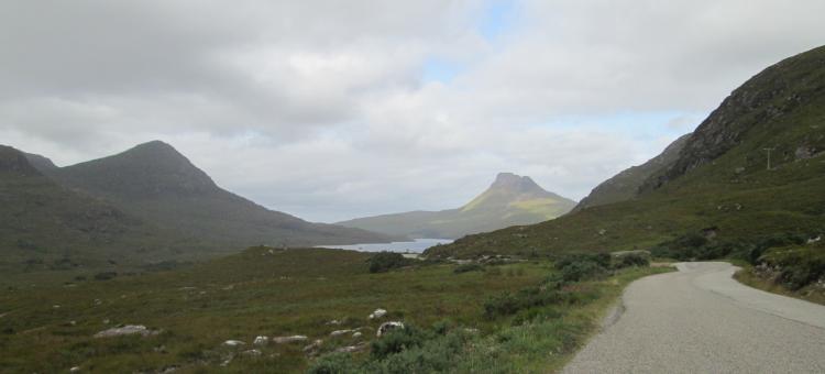 A narrow road winds alongside steep hills and mountains and lochs near Achiltibuie