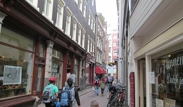 A narrow street with cafes, bicycles, tourists and shoppers