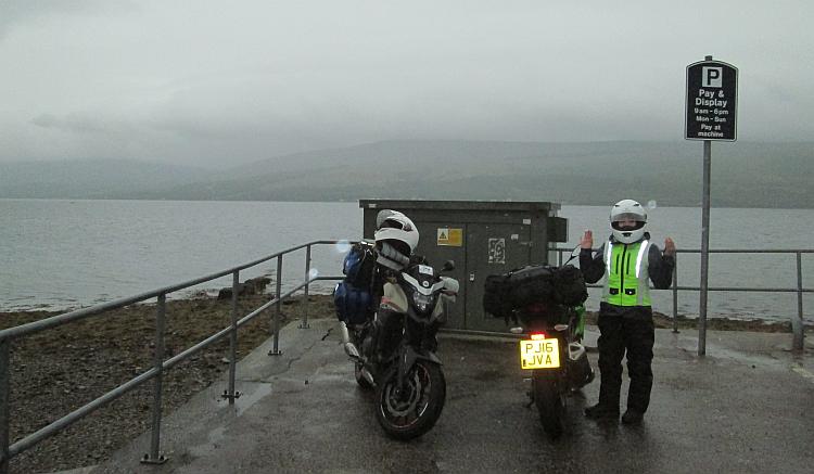 Sharon stands next to the bikes with her hands up in the pouring rain at inverary